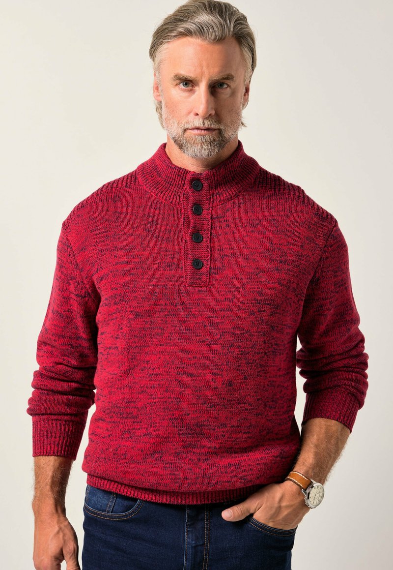 Roter strukturierten Strickpullover mit hohem Kragen, ausgestattet mit einer Knopfleiste und gerippten Bündchen. Wird mit dunklen Jeans getragen.