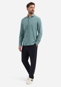 Lichtblauwe langemouwen button-up shirt met een kraag, gecombineerd met marineblauwe broek en witte sneakers. Zachte stof, relaxte pasvorm, subtiele stikdetails.