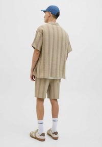 Beige rövid ujjú ing és hozzá illő, textúrázott mintás rövidnadrág. Kiegészítők között szerepel egy kék sapka és beige sportcipő fehér zoknival.