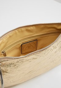 Złota, pomarszczona metaliczna kopertówka z gładkim, złotym satynowym wnętrzem. Posiada zamek błyskawiczny i wewnętrzną kieszeń z metką. Okrągłe metalowe okucia.