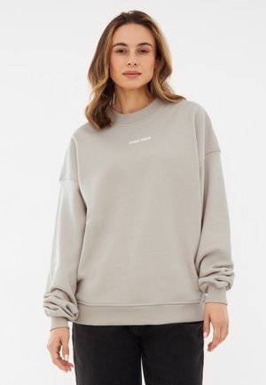 Lys grå sweatshirt med en afslappet pasform, ribbede manchetter og en rund halsudskæring. Funktioner diskret hvid branding på brystet.