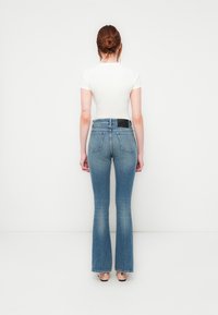 Maglietta bianca aderente a maniche corte abbinata a jeans a vita alta con gamba svasata di un leggero blu, con una sfumatura delicata e tasche posteriori.