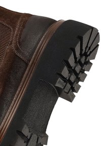 Bruine suède laars met een donkere rubberen zool en diepe grip, een elastische zijpaneel en contrasterende bruine leren afwerking.