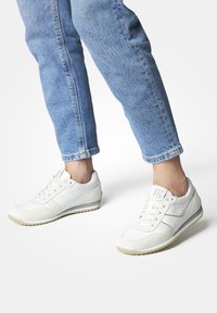 Baskets de sport blanches avec une surface lisse et texturée et des accents gris clair, dotées d'un design à lacets et d'une semelle en caoutchouc segmentée.