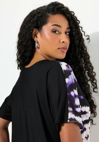 Blusa negra y de teñido anudado con mangas cortas; presenta un tejido negro y paneles con un patrón en púrpura y blanco; textura suave y ajuste relajado.
