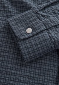 Camicia a maniche lunghe blu scuro con motivo a quadri, tessuto strutturato e bottone in plastica bianca sul polsino.