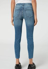 Fittade blå denimjeans med midja i normalhöjd, femficksdesign och rå nederkant vid ankeln. Tyget visar en blekt struktur och subtil sömnad.