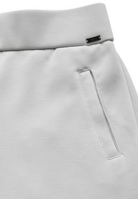 Pantalon de survêtement gris clair avec une texture lisse, doté d'une large ceinture, de poches latérales et d'un petit détail logo noir.