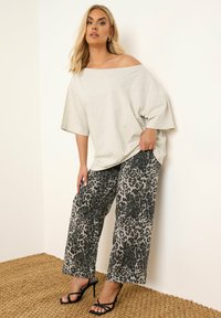 Top ligero gris claro sin hombros combinado con pantalones de corte holgado de estampado de leopardo en tonos de gris, negro y blanco. Sandalias de tacón alto negras.