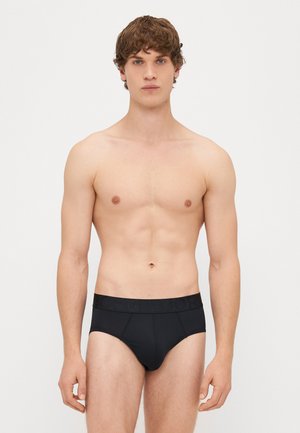 Juodi trumpi apatiniai su megztu juosmuo, kuriame įspausta logotipas. Medžiaga atrodo lygi, prigludęs dizainas pabrėžia figūrą.