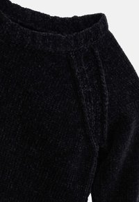 Czarny sweter o fakturowanej powierzchni wykonany jest z miękkiego, tkającego materiału, ma żebrowany dekolt oraz subtelne detale szycia na ramionach.