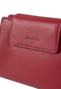 Rote Lederbörse mit strukturiertem Finish, ausgestattet mit einer vorderen Klappe und geprägtem "MAÎTRE"-Logo. Sichtbare Nähte entlang der Kanten.