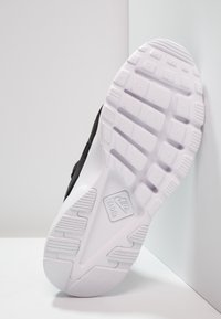 Black sneaker with a textured upper and white rubber sole. Features grooves and patterns for grip. Nike Air logo visible on the sole.