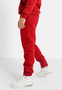 Rode katoenen sweatpants met elastische boorden, zijzakken en subtiele branding, gecombineerd met witte sport sneakers.
