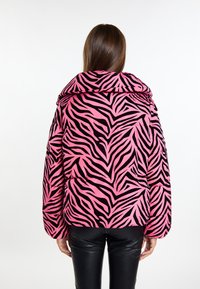 Giacca imbottita rosa con strisce zebrate nere, caratterizzata da un ampio colletto e texture trapuntata, indossata sopra pantaloni neri.