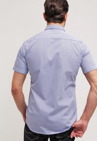 Košile s krátkým rukávem, modrý kostkovaný vzor, tkaná látka, standardní límec, zakřivený spodní lem, jediné zadní sedlo, minimalistický design.