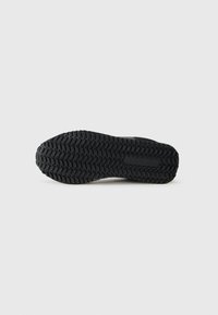 Semelle de chaussure en caoutchouc noir présentant un motif de bande de roulement profond pour une meilleure adhérence. Le design est lisse, avec une forme arrondie et sans marquage visible.
