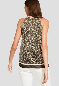 Blouse marron sans manches avec un motif à pois, détail dos ajouré et ourlet blanc contrastant. Le tissu semble lisse et léger.