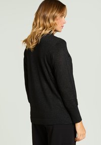 Czarny dzianinowy kardigan z delikatnym połyskiem, długimi rękawami i swobodnym krojem. Posiada okrągły kołnierz i prosty dół.