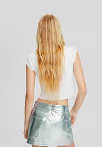 T-shirt blanc court avec des manches courtes associé à une mini-jupe argentée métallique dotée de quatre poches et d'une finition texturée.