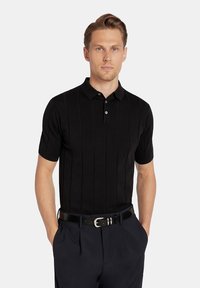 Czarna koszulka polo z krótkim rękawem o teksturowanym wzorze, dopasowany krój, z dwoma guzikami na listwie, w zestawie z granatowymi spodniami i czarnym paskiem.
