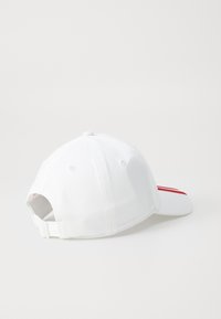 Hvid baseballkasket med justerbar rem, røde striber på den forreste skygge, vist fra bagsiden på en hvid baggrund.