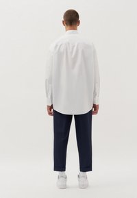 Witte pinstripe overhemd met een gebogen zoom, knoopmanchetten en een rugplooi, gecombineerd met marineblauwe broek en witte sneakers. Eenvoudig, schoon ontwerp.