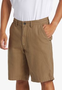 Pantalones cortos de algodón marrón con un diseño de pierna recta, bolsillos frontales, cierre de botón y una cintura plana.
