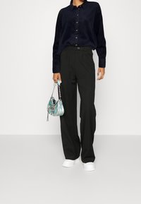 Camicia a bottone in corduroy blu navy, pantaloni neri a vita alta, sneakers bianche e una piccola borsa iridescente con hardware in argento.
