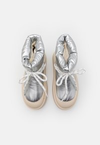 Botas estilo puff de color plata con un interior suave, cordones blancos y una suela de goma beige. La parte superior tiene un acabado brillante y reflectante.
