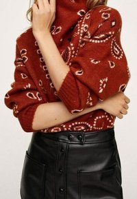 Przytulny sweter w kolorze rdzy z wysokim kołnierzem, z białymi wzorami, zestawiony z czarną spódnicą z sztucznej skóry z detalami guzików.