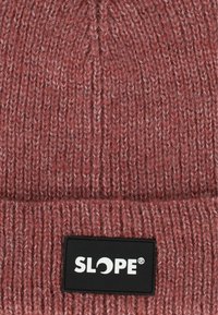 Neulottu pipo pölyroseassa värissä, jossa on musta tyylikäs etiketti, jossa lukee "SLOPE" valkoisella. Paksu ribbitekstuuri koko pinnalla.