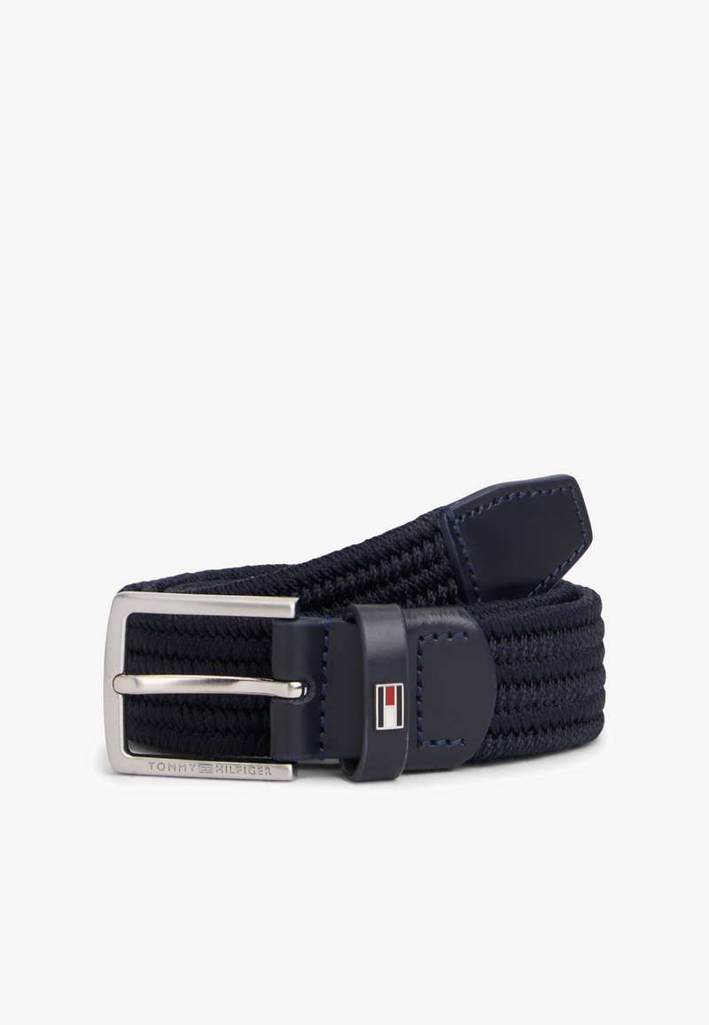 Ζώνη από υφασμάτινο ύφασμα σε ναυτικό μπλε χρώμα με ασημένια ορθογώνια αγκράφα και δερμάτινες λεπτομέρειες που φέρουν ένα μικρό κόκκινο, λευκό και μπλε λογότυπο.