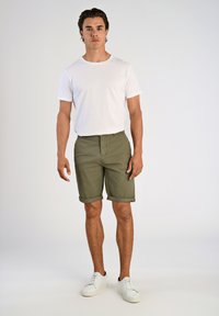 Pantalones cortos verde oliva con puños, combinados con una camiseta básica blanca de cuello redondo. Llevados con zapatillas blancas, con un diseño y textura minimalistas.
