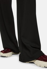 Black wide-leg pants with a smooth texture, paired with red glittery sneakers featuring a chunky sole and cream accents.