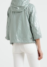 Světlezelená, lesklá bunda s kapucí a tříčtvrtečními rukávy. Má zaoblený lem a štítek s logem blízko spodního okraje. Nalezena přes bílé džíny.