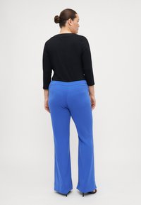 Haut noir à manches trois-quarts associé à un pantalon large bleu lisse. Le pantalon présente une taille plate à l'avant et un léger éclat.