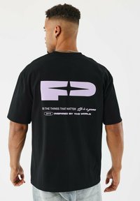 Camiseta de algodón negra con un gran gráfico de color púrpura claro en la parte posterior con texto. Corte holgado, mangas cortas y diseño de cuello redondo.