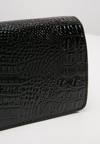 Borsetta nera con effetto coccodrillo, dalla superficie lucida e texture. Forma rettangolare con bordi puliti. Nessuno hardware o dettagli visibili.