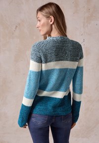 Stickad tröja med horisontella ränder i nyanser av blått, vitt och teal. Den har en rund halsringning och ribbad textur på ärmslut och fåll.