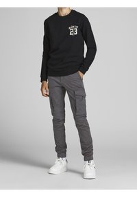 Czarna bluza z nadrukiem "BLACK CAT 23"; zestawiona z szarymi spodniami cargo z kieszeniami bocznymi; całość dopełniają białe sneakersy.