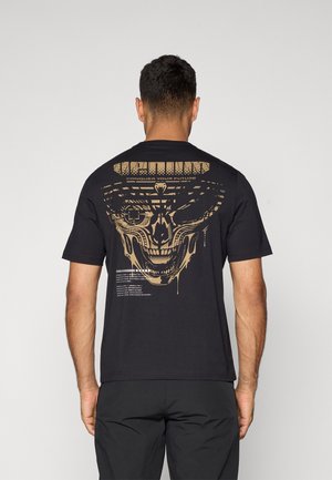 Black t-shirt featuring a large gold graphic of a skull and text on the back. Short sleeves and a regular fit, made of soft fabric.