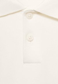 Nahaufnahme eines weißen Poloshirtkragens mit zwei weißen Knöpfen, die auf einem strukturierten Stoff befestigt sind.