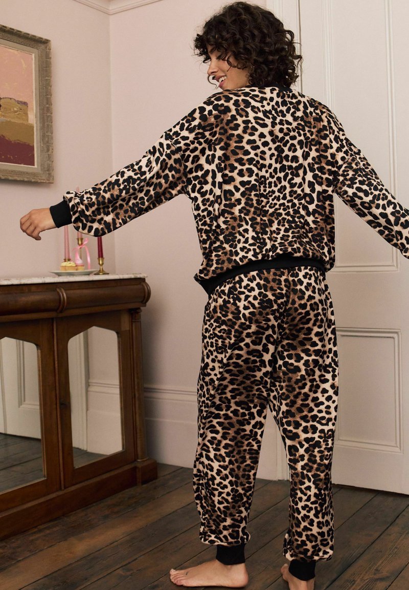 Sada pohodlného oblečení s leopardím potiskem vyrobena z měkké tkaniny, obsahující volnější top s černými manžetami a odpovídající kalhoty s elastickými kotníky.