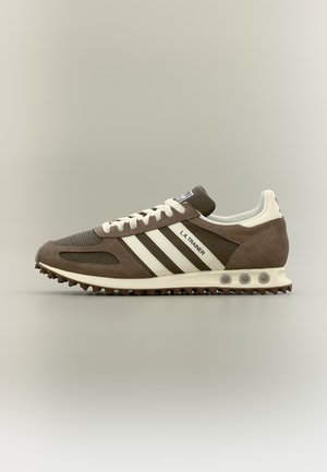 Brauner und cremefarbener Adidas LA Trainer Sneaker mit weißen Schnürsenkeln, drei weißen Streifen und einer strukturierten Sohle, seitlich auf neutralem Hintergrund gezeigt.