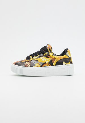 Baskets avec un motif floral coloré en jaune, orange et gris. Dotées d'un lacet noir texturé et d'une semelle en caoutchouc blanche avec un motif clé grecque.