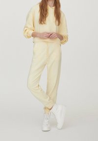 Żółta polarowa bluza z kapturem i dopasowane dresy z talią na sznurki, w połączeniu z białymi trampkami za kostkę, charakteryzującymi się luźnym krojem.