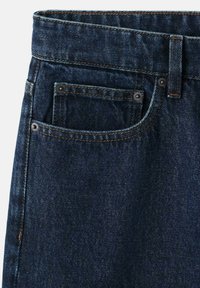 Jean en denim bleu foncé en gros plan montrant la poche avant, la poche à monnaie, la passants de ceinture et les détails de coutures contrastantes.