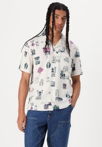 Short-sleeve, button-up shirt with a white base, featuring various multicolored graphic prints and a relaxed fit.
