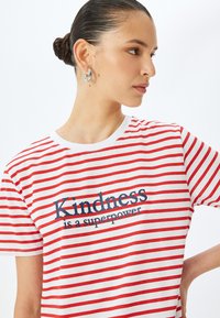 Rød- og hvidstribet t-shirt med rund halsudskæring og korte ærmer, præget med teksten "Venlighed er en superkraft" i marineblå.